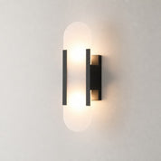 Warm glowing black wall sconce with frosted rounded vertical diffuser on a neutral wall.
