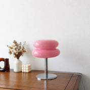 Glossy pink double-cushion lamp with chrome stem and round base on a wooden tabletop.