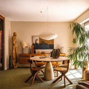 Round stone pedestal dining table with wooden chairs in a warm plant-filled living room.