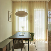 Oval ribbed paper pendant lamp above a dining table in a sunlit room.