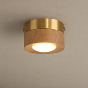 Round flush mount ceiling light with wood body, brass rim, and glowing white diffuser.