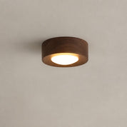 Round wooden flush mount ceiling light with warm glowing diffuser on a plain gray ceiling.
