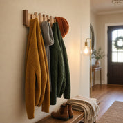 Wooden wall hooks hold a mustard cardigan, gray scarf, green quilted jacket, and orange knit beanie.