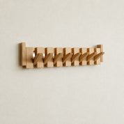 Wooden wall-mounted coat rack with angled pegs on a pale wall.