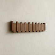 Wooden wall-mounted rack with staggered vertical slats on a plain cream wall.