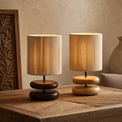 Two glowing wooden table lamps with ribbed cylindrical shades on a rustic wood surface.
