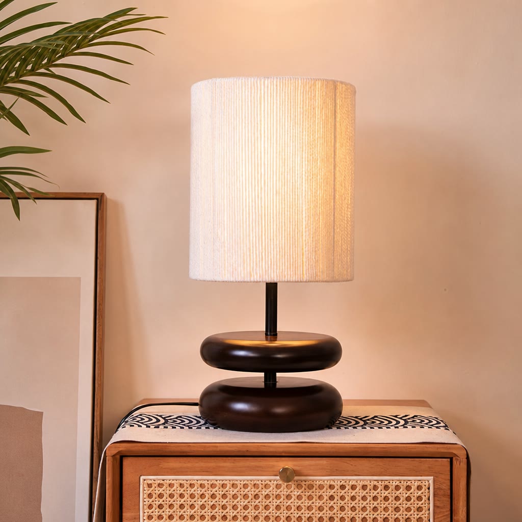 Warm table lamp with a white ribbed shade and dark rounded base on a wooden cane-front nightstand.