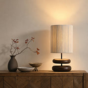 Warm table lamp with beige fabric shade and dark stacked wooden base on a rustic console.