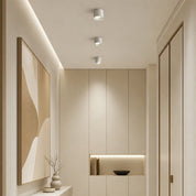 Minimalist room ceiling with three white cylindrical spotlight fixtures above beige wall panels.