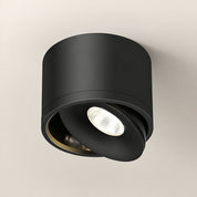 Black cylindrical adjustable ceiling spotlight with a tilted illuminated lens.