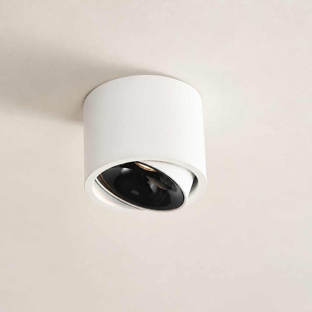 White cylindrical ceiling spotlight with a tilted black lens on a plain ceiling.
