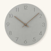 Round gray wall clock with thin black numbers and wooden hands on a light neutral background.