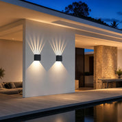 Two black cube wall lights cast geometric beams on a white exterior wall.