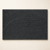 Charcoal rectangular ribbed rug with raised curved arc patterns on a light surface.