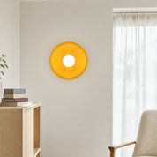 Yellow circular wall lamp with a white center mounted on a light living room wall.
