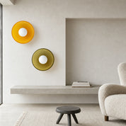 Two circular wall lights, one amber and one olive, displayed in a minimalist living room.