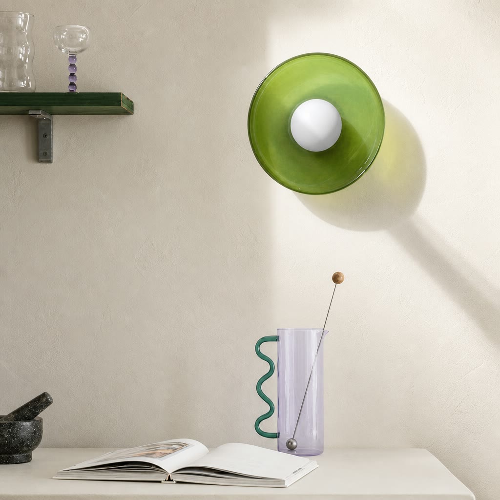 Green wall lamp above a lavender vase with wavy teal handle on a white tabletop.