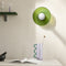 Green wall lamp above a lavender vase with wavy teal handle on a white tabletop.