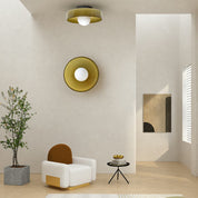 White lounge chair sits below matching amber circular wall and ceiling lights in a minimalist room.