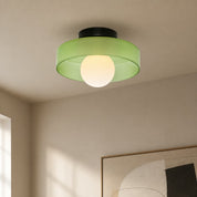 Green flush mount ceiling light with translucent shade and glowing round bulb.