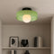 Green flush mount ceiling light with black base and glowing white globe above a neutral shelf.