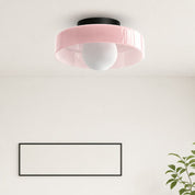 Pink flush mount ceiling light with a white globe bulb and black ceiling cap.