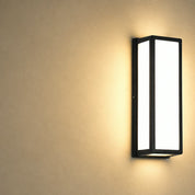 Black rectangular wall sconce with glowing frosted panels on a warm beige wall.