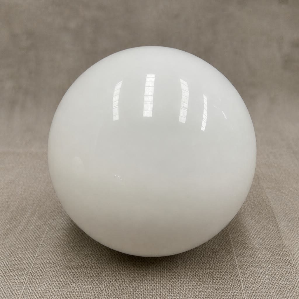Glossy white spherical lamp shade on a neutral fabric surface.