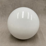 Glossy white spherical lamp shade on a neutral fabric surface.