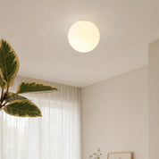 Glowing round ceiling light mounted above sheer curtains and a leafy indoor plant.