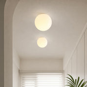 Two glowing spherical ceiling lights illuminate a minimalist hallway with white walls and a plant.