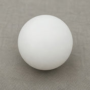 Smooth white spherical ball resting on a muted gray fabric surface.