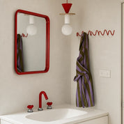Red bathroom mirror, faucet, pendant light, and wavy towel hook above a white sink.
