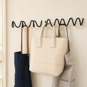 Black wavy wall hook rack holding cream, navy, and gray bags.