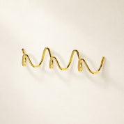 Polished gold wavy wall hook rack on a clean light background.
