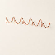 Rose gold wavy wall rack with multiple rounded hooks on a clean white surface.