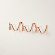 Rose gold wavy wall-mounted hook rail on a clean white surface.