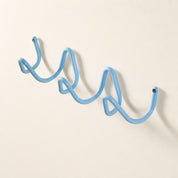 Light blue wavy wall-mounted hook rack with screw caps on a plain wall.