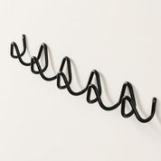 Black wavy metal wall rack with multiple curved hooks on a plain light wall.