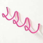 Pink wavy wall-mounted hook rack with screw ends on a white wall.