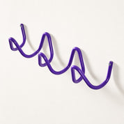 Purple wavy wall-mounted metal rack with visible end screws on a plain light wall.