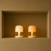 Two small glowing mushroom lamps, one white and one peach, sit side by side on a recessed shelf.