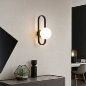 Black oval wall sconce with a glowing white globe above a modern console.