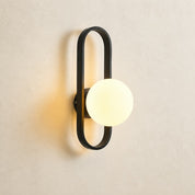 Modern wall sconce with a black oval frame and glowing round globe on a light textured wall.