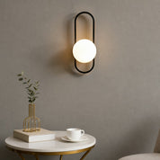 Black oval wall sconce with a glowing white globe above a minimalist side table.