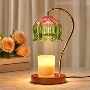Glowing candle warmer lamp with green and pink glass shade on a wooden base.