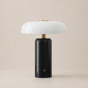 Glossy black cylindrical table lamp with a white rounded shade and brass accents.