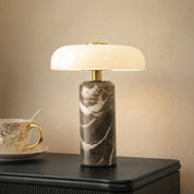 Brown marble table lamp with a glowing white shade and brass accents on a dark tabletop.