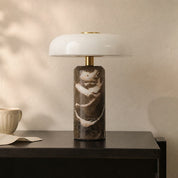 Marble table lamp with a white dome shade and brass accents on a dark bedside table.