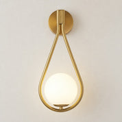 Brass teardrop wall sconce with a glowing white globe shade on a light neutral wall.